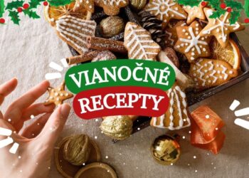 Tanier plný tradičných vianočných koláčikov ozdobených bielou polevou, obklopený vianočnými ozdobami, škoricou a sušenými pomarančmi. Ruka siaha po hviezdičkovom koláčiku.