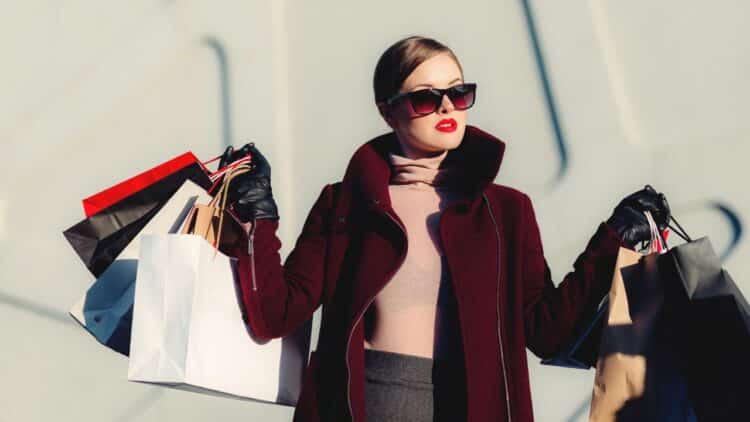 Žena v elegantnom kabáte s nákupnými taškami, symbolizujúca nákupnú horúčku počas Black Friday.