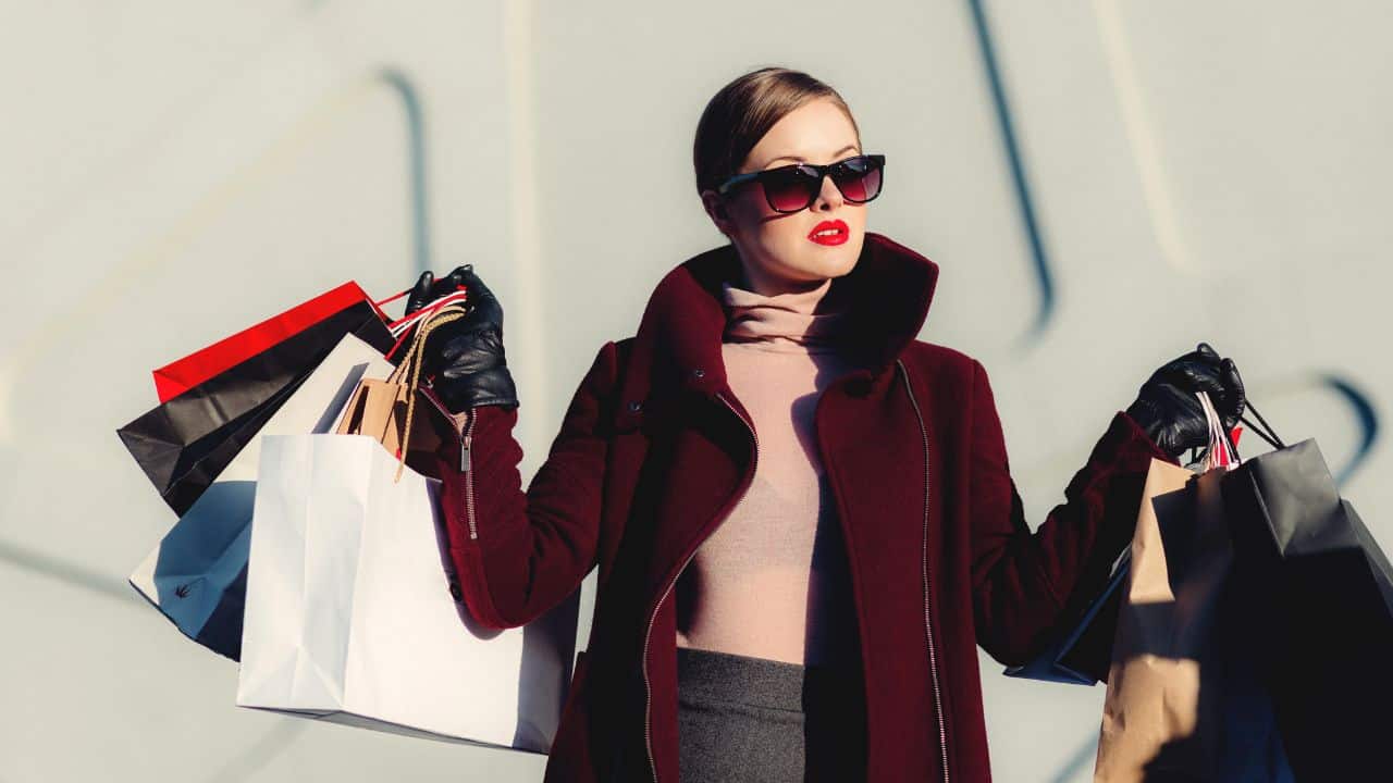 Žena v elegantnom kabáte s nákupnými taškami, symbolizujúca nákupnú horúčku počas Black Friday.