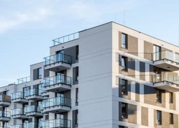 Moderný bytový dom s balkónmi a farebnou fasádou osvetlený slnečným svetlom.