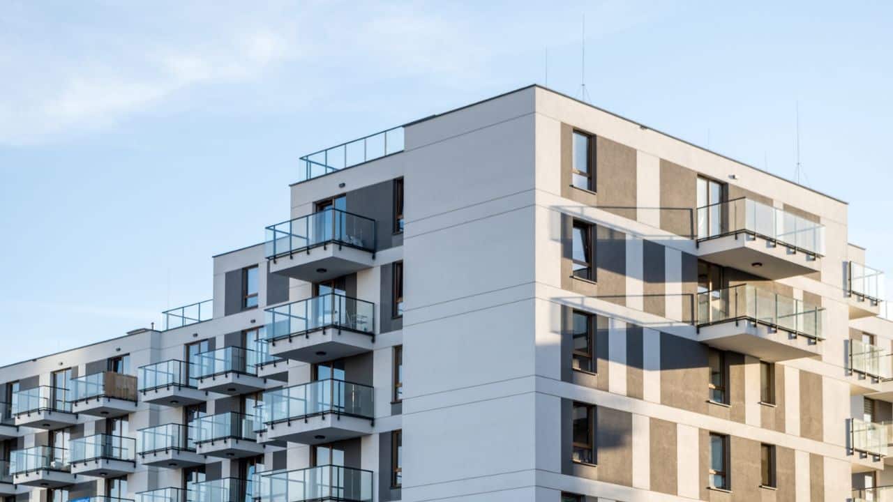 Moderný bytový dom s balkónmi a farebnou fasádou osvetlený slnečným svetlom.