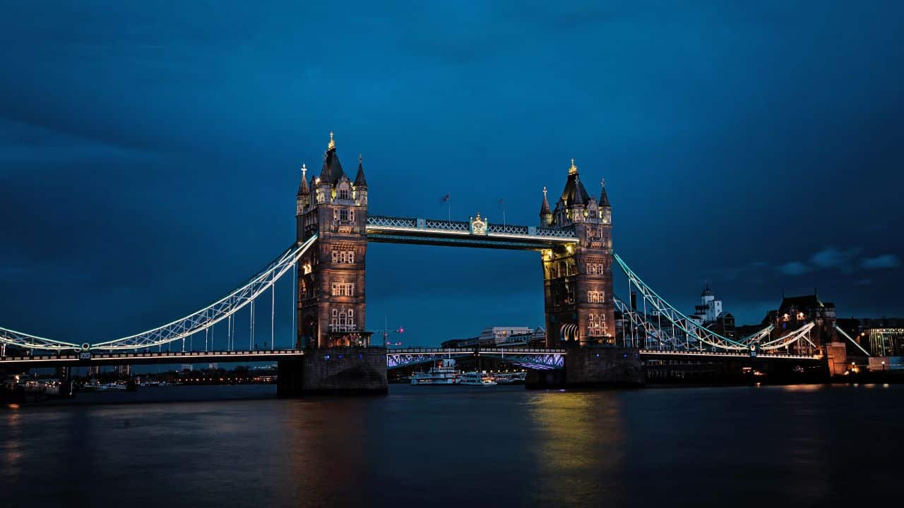 Večerný pohľad na osvetlený Tower Bridge v Londýne s tmavomodrou oblohou v pozadí.