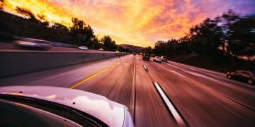 Auto jazdí po diaľnici pri západe slnka, s farebnou oblohou a hustým okolitým stromami.