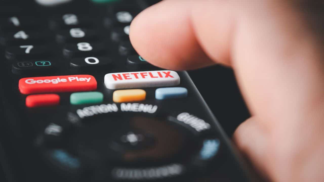 Ruka stláčajúca tlačidlo Netflix na diaľkovom ovládači so zreteľnými tlačidlami Google Play, Netflix a farebnými možnosťami.