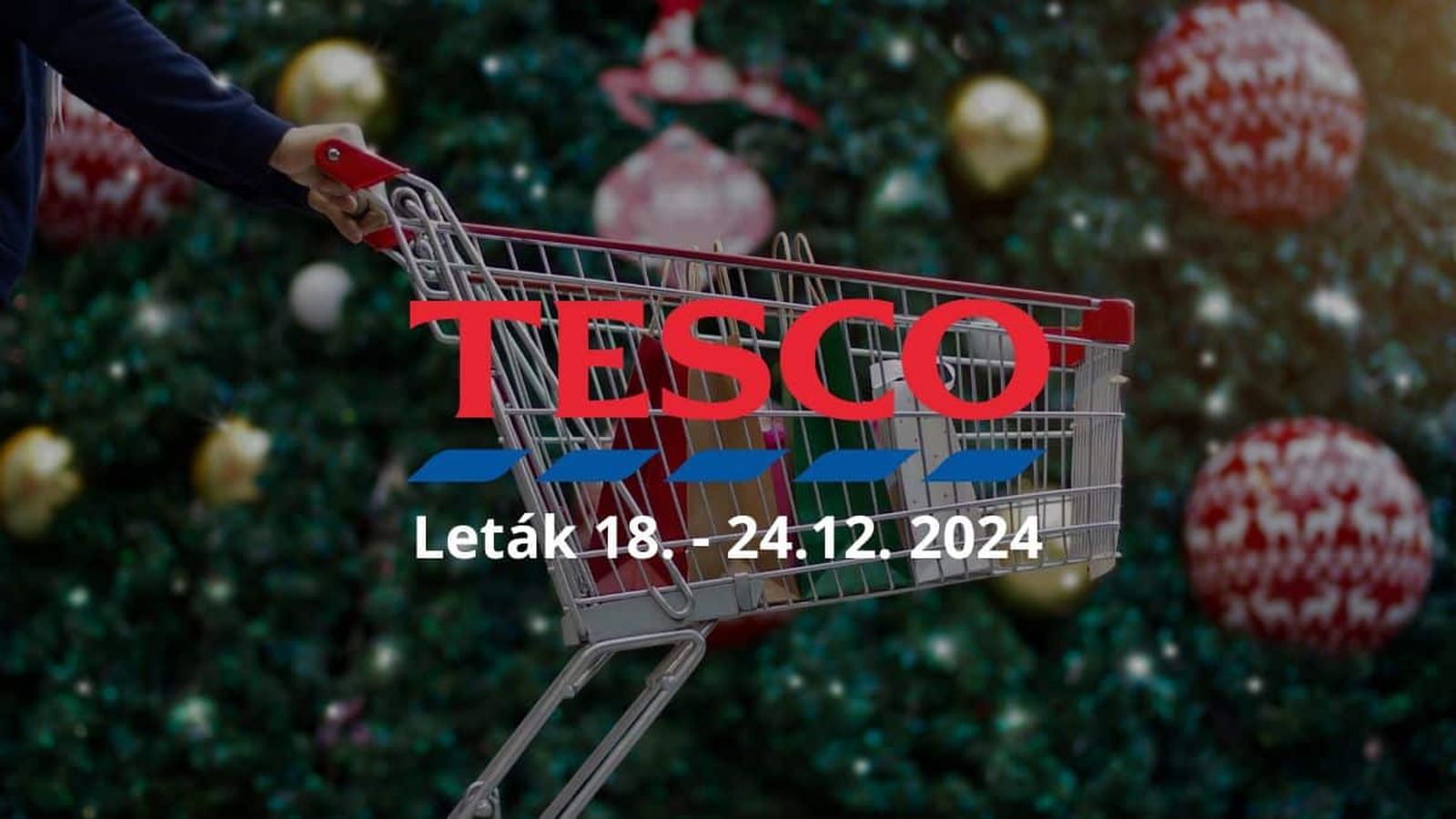 Vianočný nákupný košík pred vianočným stromčekom s ozdobami a textom Tesco Leták 18. - 24.12. 2024.