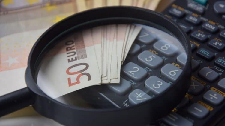 Lupa zvýrazňujúca bankovky 50 eur a kalkulačku, symbolizujúca financie a daňové povinnosti.