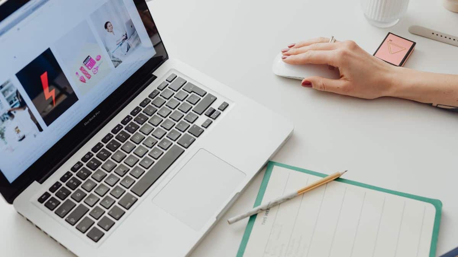 Žena pracuje na MacBook Pro pri online nakupovaní, vedľa nej je poznámkový blok a pero.
