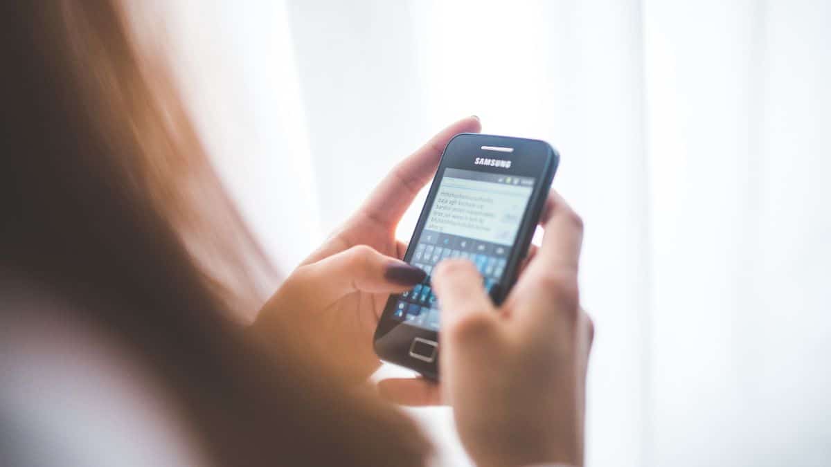 Žena píšuca SMS správu na staršom telefóne Samsung s dotykovou klávesnicou.