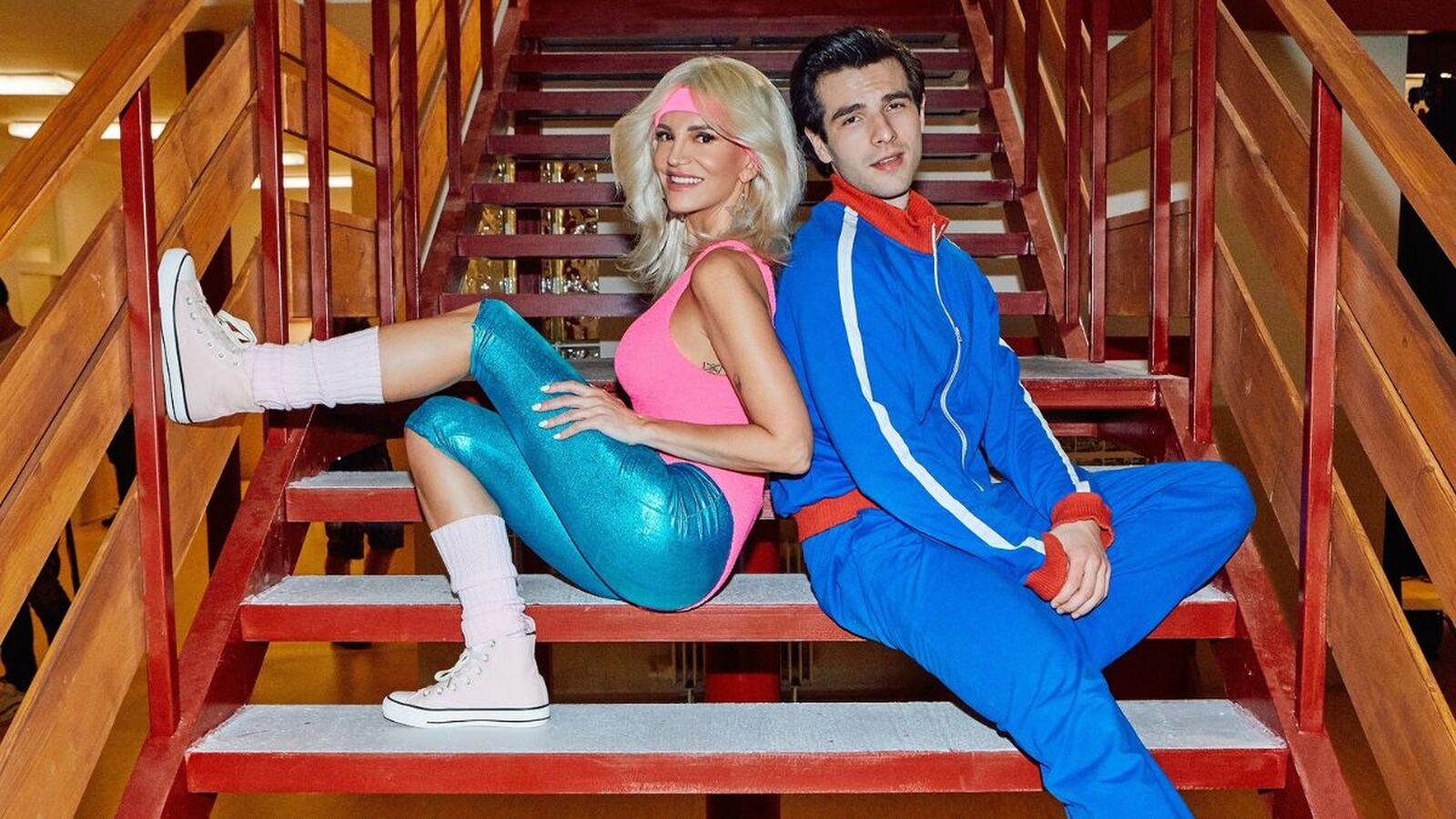 Dara Rolins v retro outfite z 80. rokov sedí na schodoch vedľa herca v modrej teplákovej súprave, zachytávajúc atmosféru videoklipu k piesni Sľub.