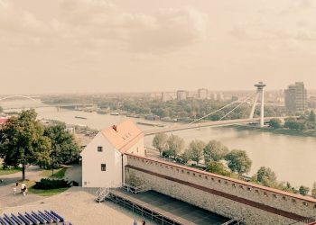 Pohľad z Bratislavského hradu na rieku Dunaj s Mostom SNP a panorámou moderného mesta v historickom tóne.